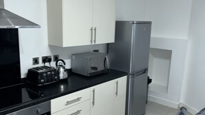 Una cocina moderna con armarios blancos, encimera negra, refrigerador de acero inoxidable y horno empotrado.