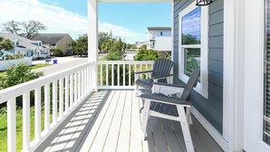 A wooden deck with two Adirondack chairs, a white railing, and a view of neighboring houses.