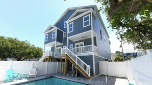 A two-story house with a swimming pool, a wooden deck, and a white fence.