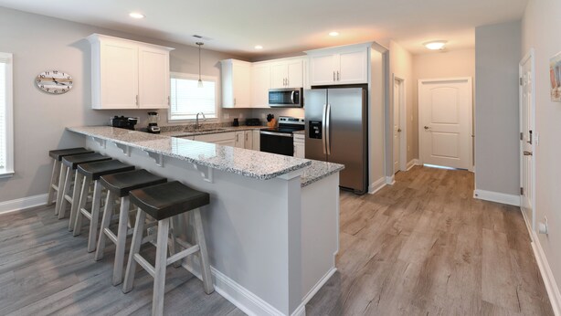 A modern kitchen with a central island, bar stools, stainless steel appliances, and light wood flooring.