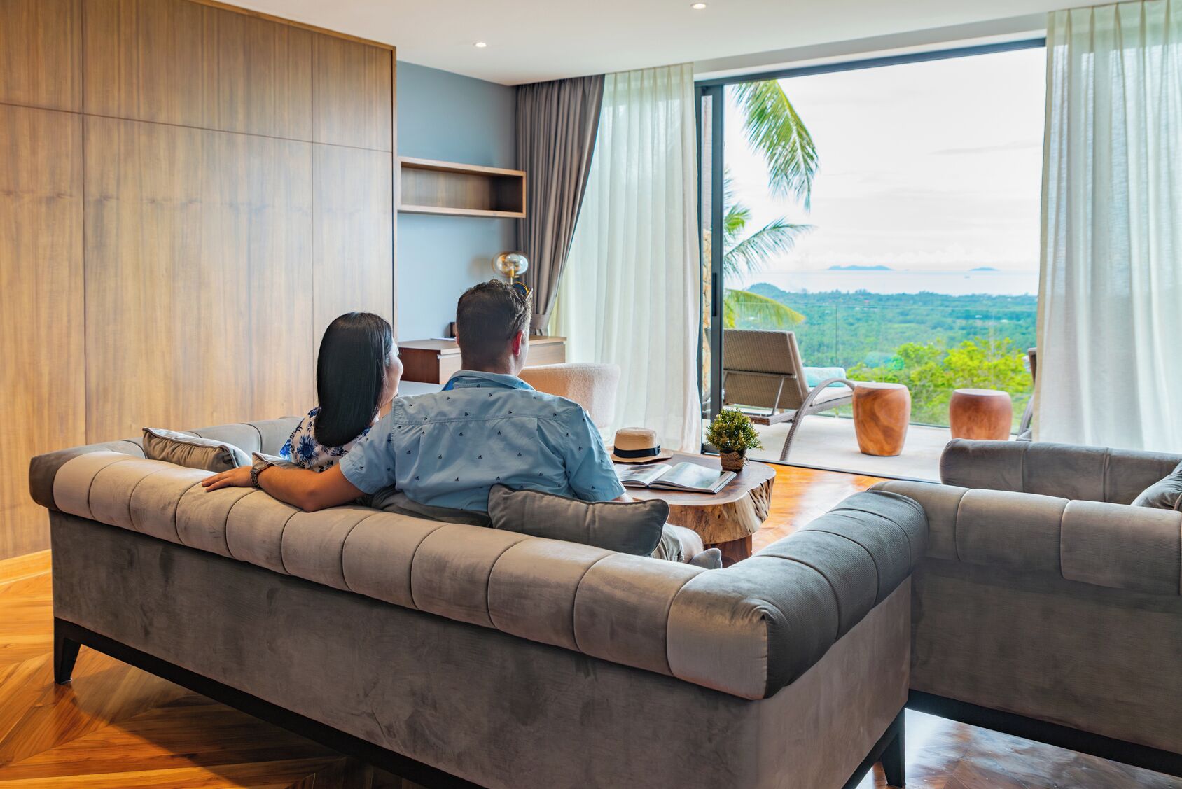 Una sala de estar moderna con un conjunto de sofás, una mesa de centro y vistas a un paisaje montañoso a través de ventanas amplias.