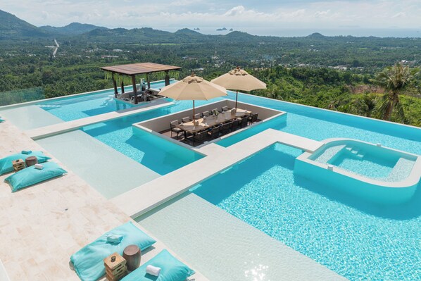 A luxurious infinity pool with a view of the mountains and a seating area with umbrellas.