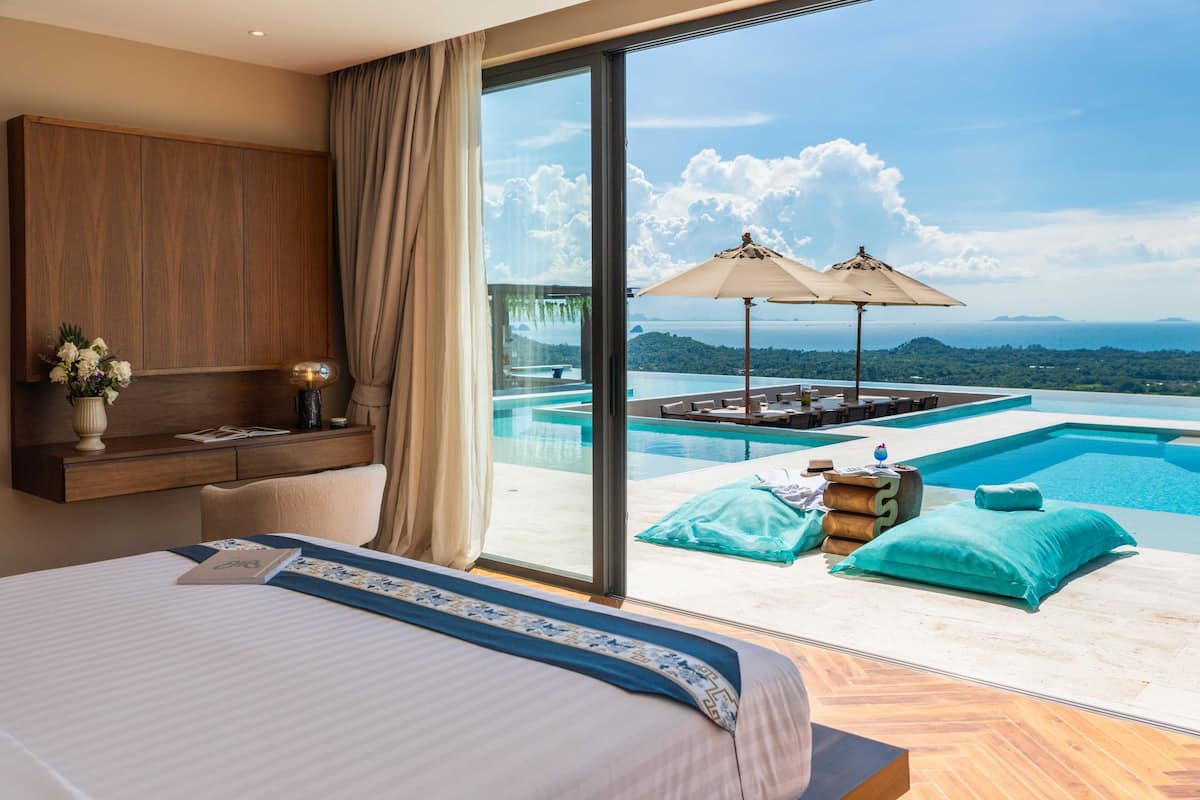 Une chambre d’hôtel avec un grand lit, une vue sur la piscine et un balcon équipé de parasols.