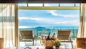 Ein Balkon mit zwei Korbstühlen, einem Tisch, einer Flasche, Gläsern und einem Buch, mit Blick auf eine Küstenlandschaft.