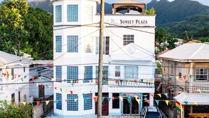 A multi-story building named 'Sunset Plaza' with a tower section, a ground-level grocery bar, and a parking area with cars. - Sunset Plaza Apartments 2 (Victoria)