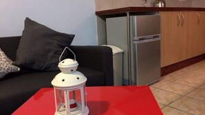 A living area with a red table, a white lantern, a black sofa, and a kitchen with a refrigerator and cabinets. - Sunset Plaza Apartments 2 (Victoria)
