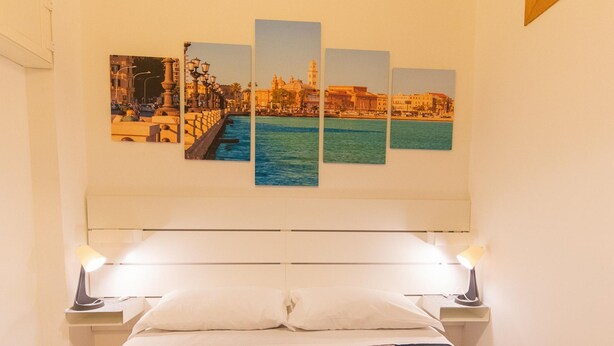 Een hotelkamer met een bed, twee bedlampen en een muur met een stadsgezicht op een kunstwerk.