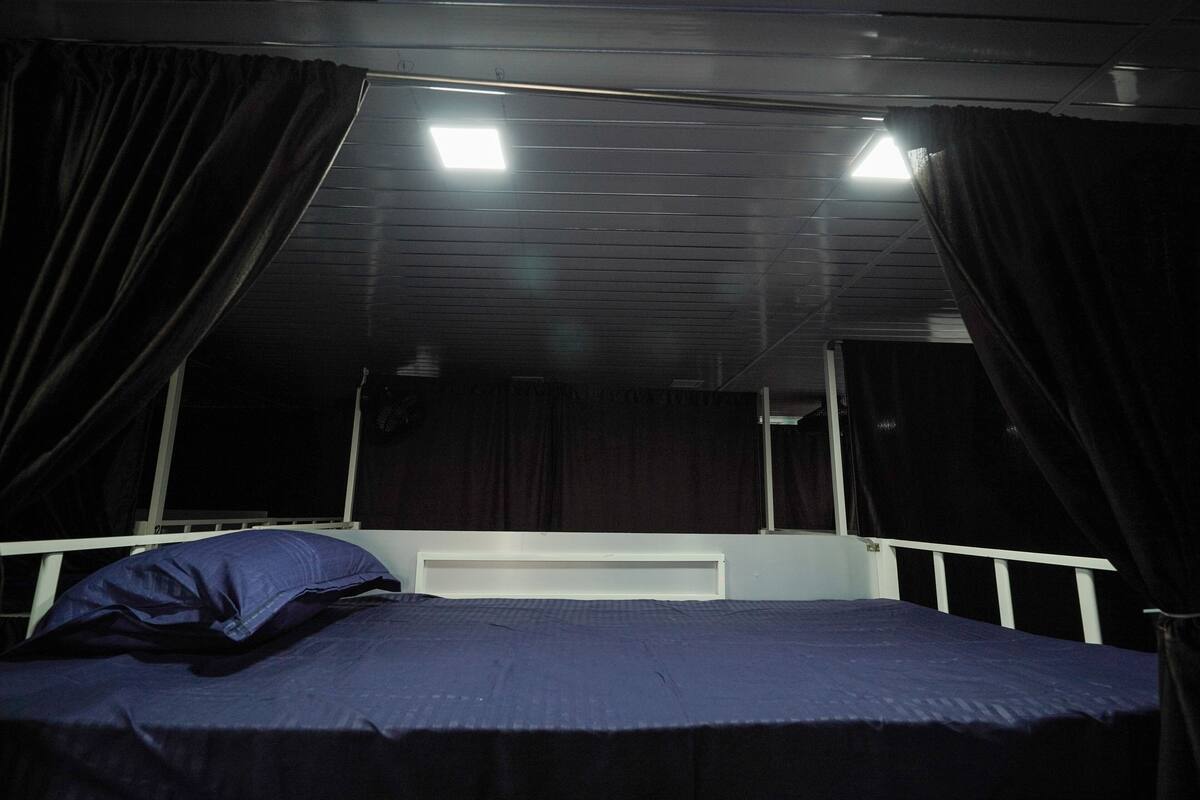 Uma cama de solteiro com cabeceira, uma janela e uma luminária no teto.