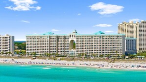 A large hotel with multiple floors, a central archway, and a beach in the foreground. - Majestic Sun A1104* Beachfront (Miramar Beach)