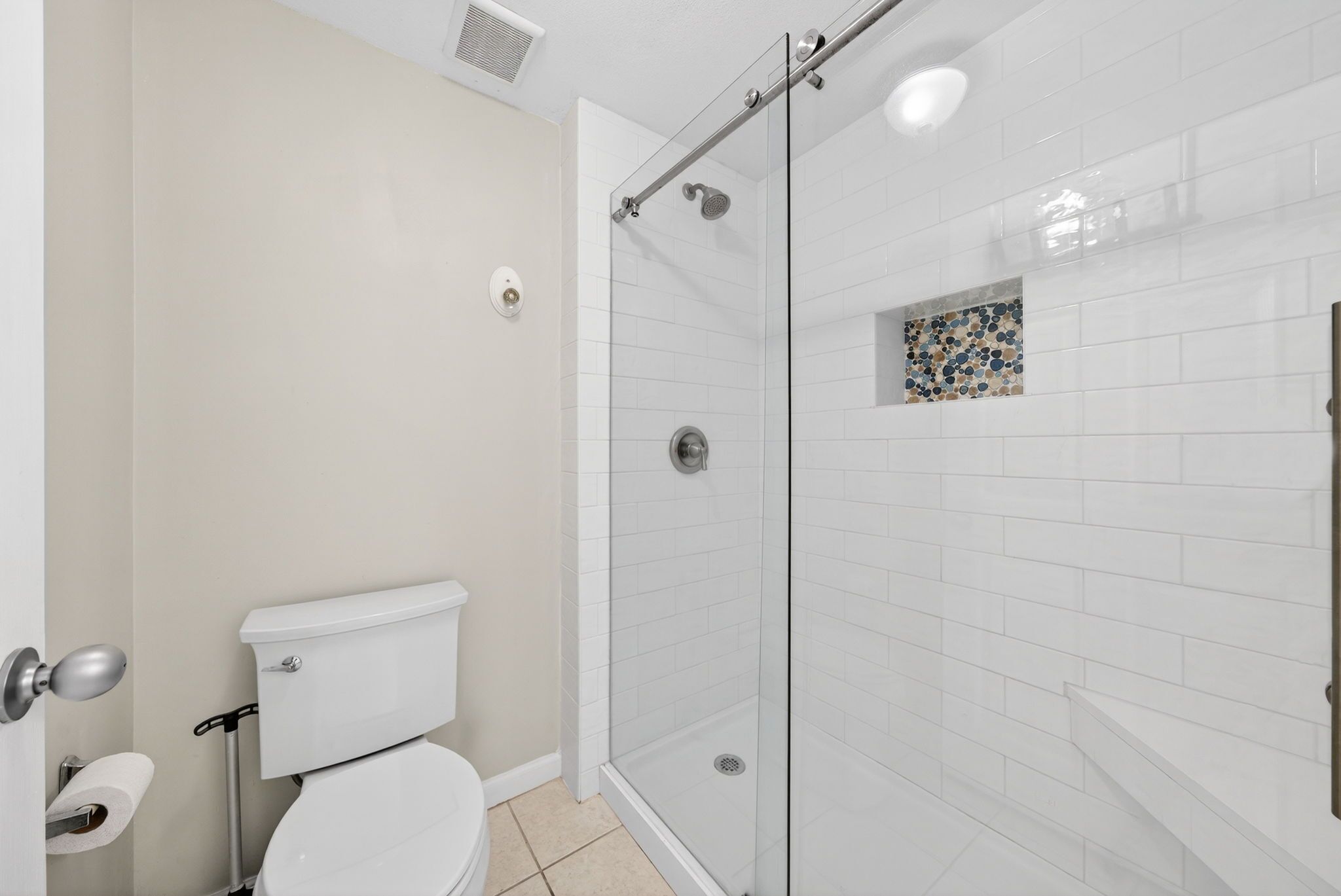 Een badkamer met toilet, een douchecabine van glas en een betegelde wand.