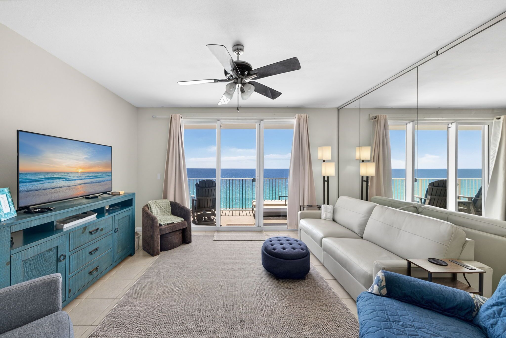 A modern living room with a television, sofa, ottoman, and a ceiling fan.