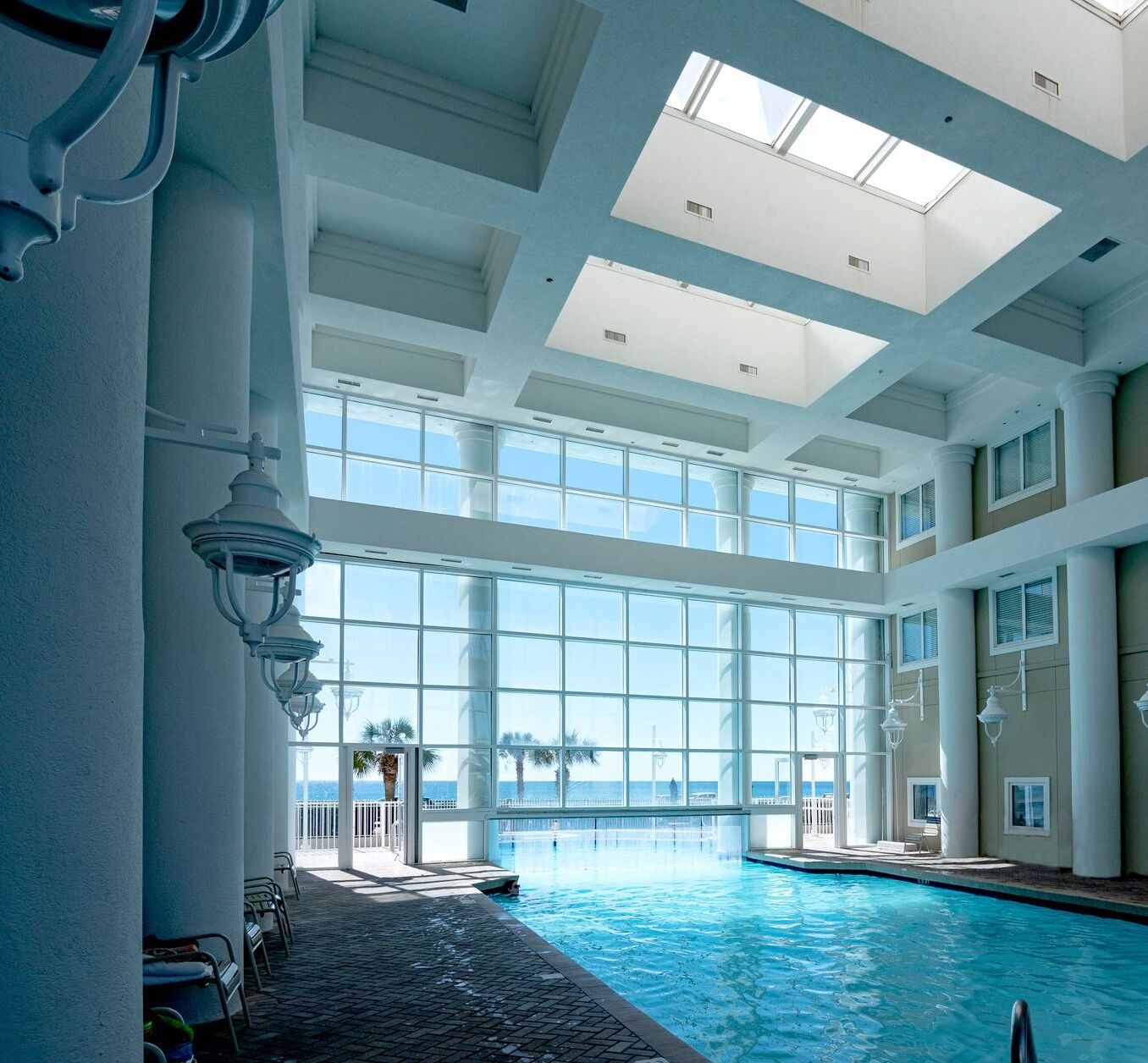 An indoor swimming pool with a view of the ocean, large windows, and a high ceiling.