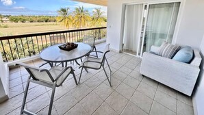 Un balcon avec une table et des chaises, un canapé et une vue sur des palmiers et un champ.