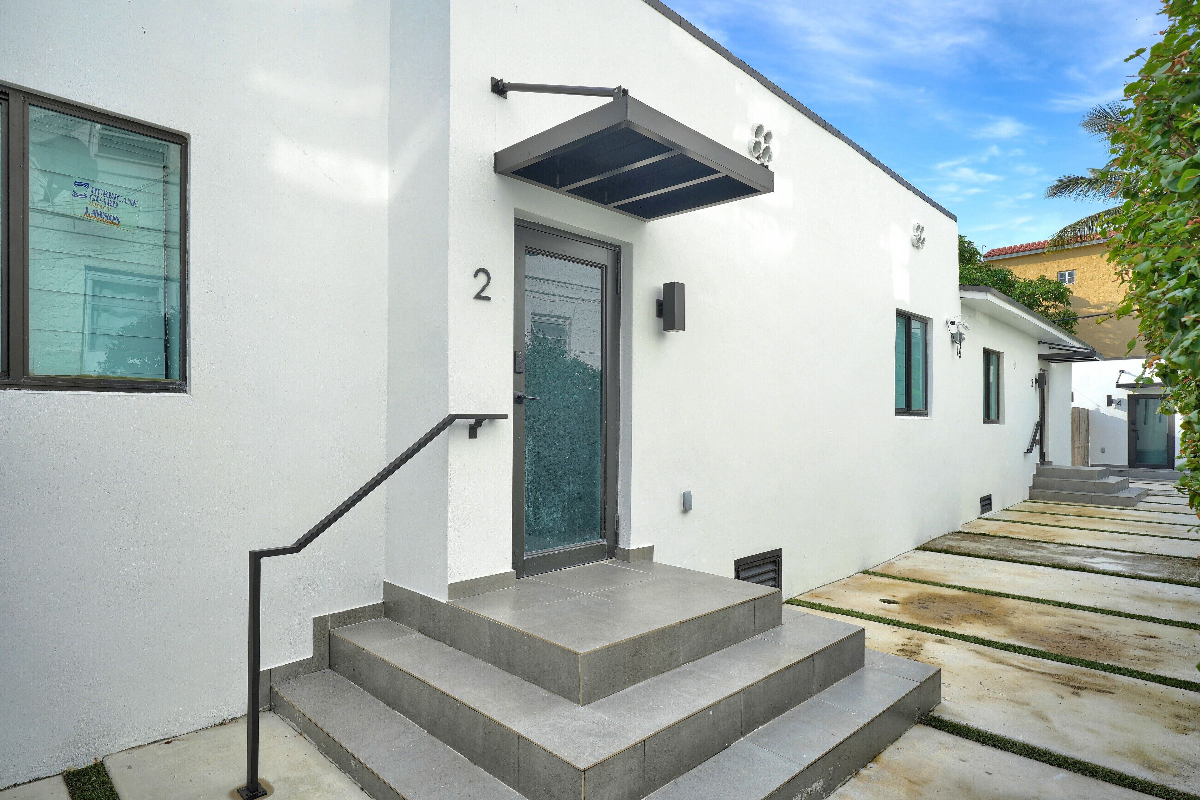 A modern building with a white exterior, a number '2' above the door, and a small set of concrete steps leading to the entrance.