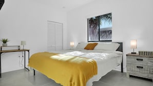 Quarto moderno com cama, mesas de cabeceira e janela com vista para árvores.