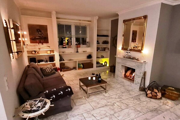 A living room with a fireplace, a sofa, a coffee table, and shelves with various items.