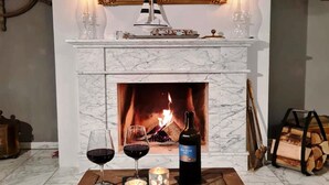 A fireplace with a lit fire, two wine glasses, a bottle of wine, and decorative items on a wooden table. - Charmante Hausvilla in Bojendorf (Bojendorf)