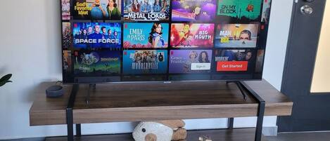 A flat-screen TV mounted on a wall with a 'COMEDY' label above it, displaying various Netflix shows.