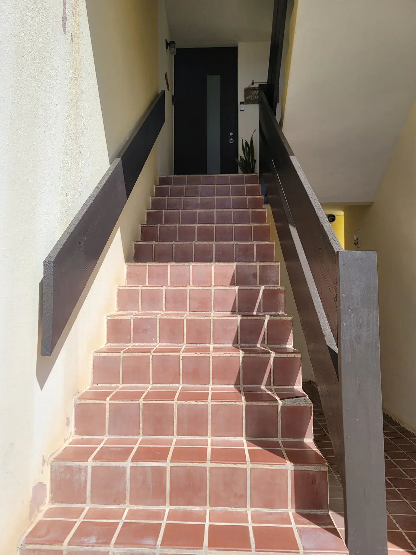 A staircase with red tiles leading to a dark door.