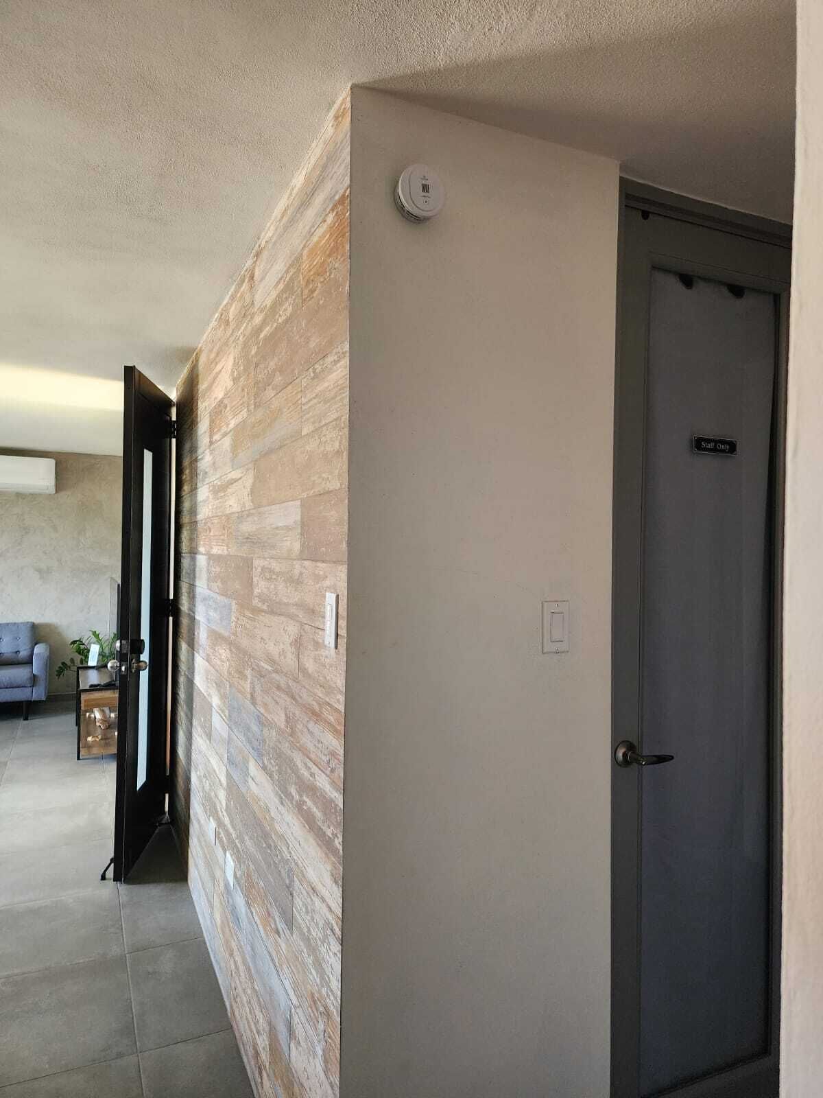 Un pasillo con pared de madera, una puerta que indica "Solo Personal" y un detector de humo instalado en el techo.