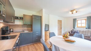 Una cuina compacta amb electrodomèstics moderns, zona de dinar amb taula per a dues persones i un espai d'estar acollidor amb sofà i coixins.