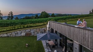 Eine Holzterrasse mit Gartenmöbeln, eine Steinmauer und Blick auf einen Weinberg und Hügel.