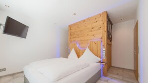 Ein Schlafzimmer mit Bett, Holz-Kopfstütze, einem angebrachten Fernseher und einem kleinen Teppich.