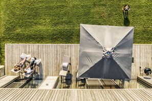 Eine Holzterrasse mit Pool, Liegestühlen und einem großen Sonnenschirm.