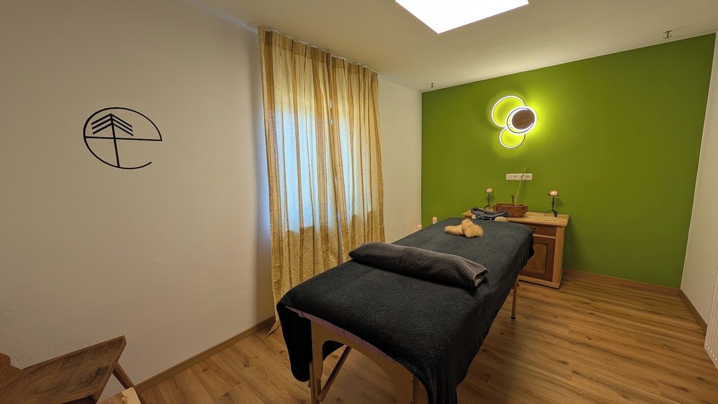A room with a bed, a wooden floor, a green wall, a neon light, and a window with curtains.
