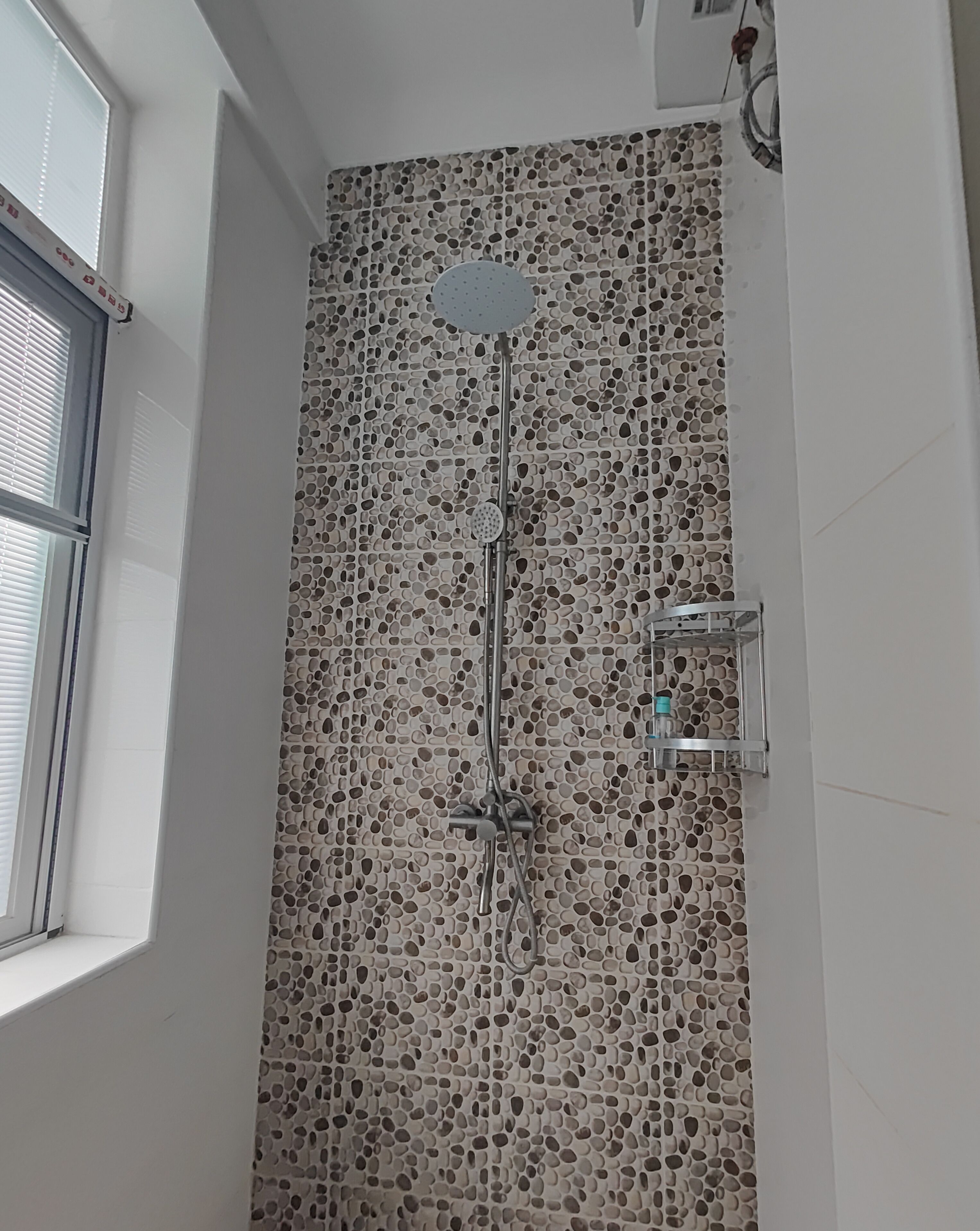 A shower with a perforated tile wall, a handheld showerhead, and a wall-mounted faucet.