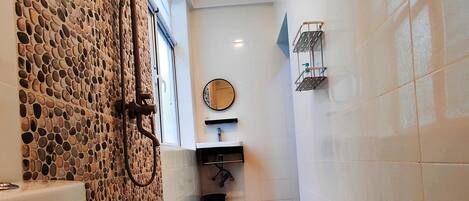 Un baño con pared de piedra, inodoro, ducha y lavamanos.