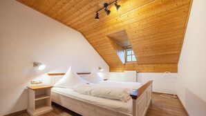 Un dormitorio con techo inclinado, estructura de cama de madera, mesita de noche y ventana con vistas al exterior.