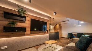 A modern living room with a wooden accent wall, a flat-screen TV, and a seating area with a sofa and chairs. - Apartment with Private Spa (Breitenberg)