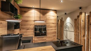 A modern kitchen with wooden cabinetry, a built-in oven, a coffee machine, and a central island with a black countertop. - Apartment with Private Spa (Breitenberg)