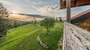 A wooden balcony overlooking a grassy field with a tree, a stone wall, and a distant view of mountains. - Apartment with Private Spa (Breitenberg)