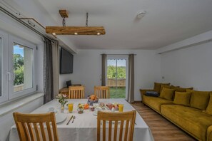 Una zona de menjador amb una taula preparada per esmorzar, un sofà i un televisor fixat a la paret.