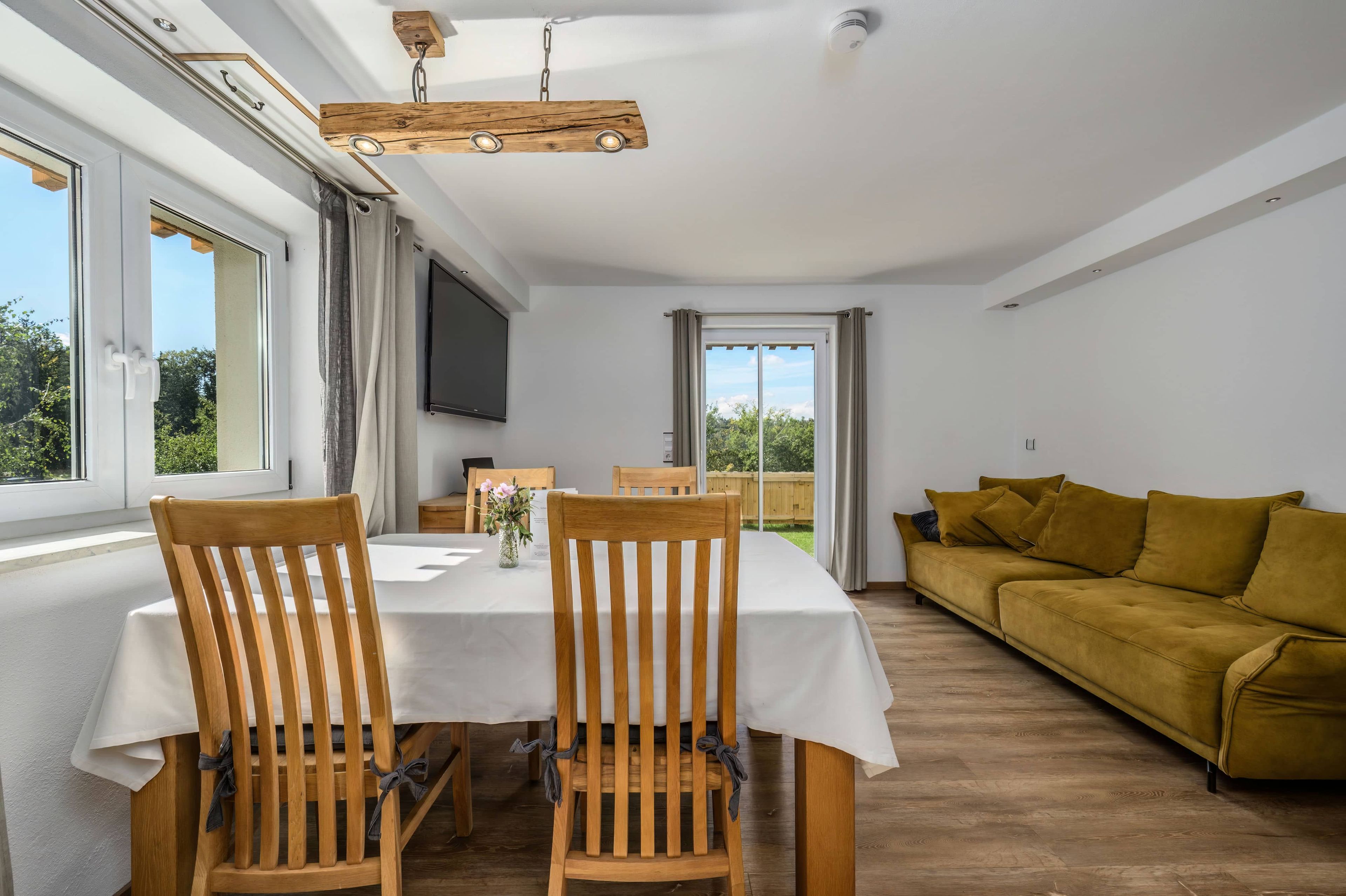 A dining area with a table and chairs, a sofa, and a television on the wall.