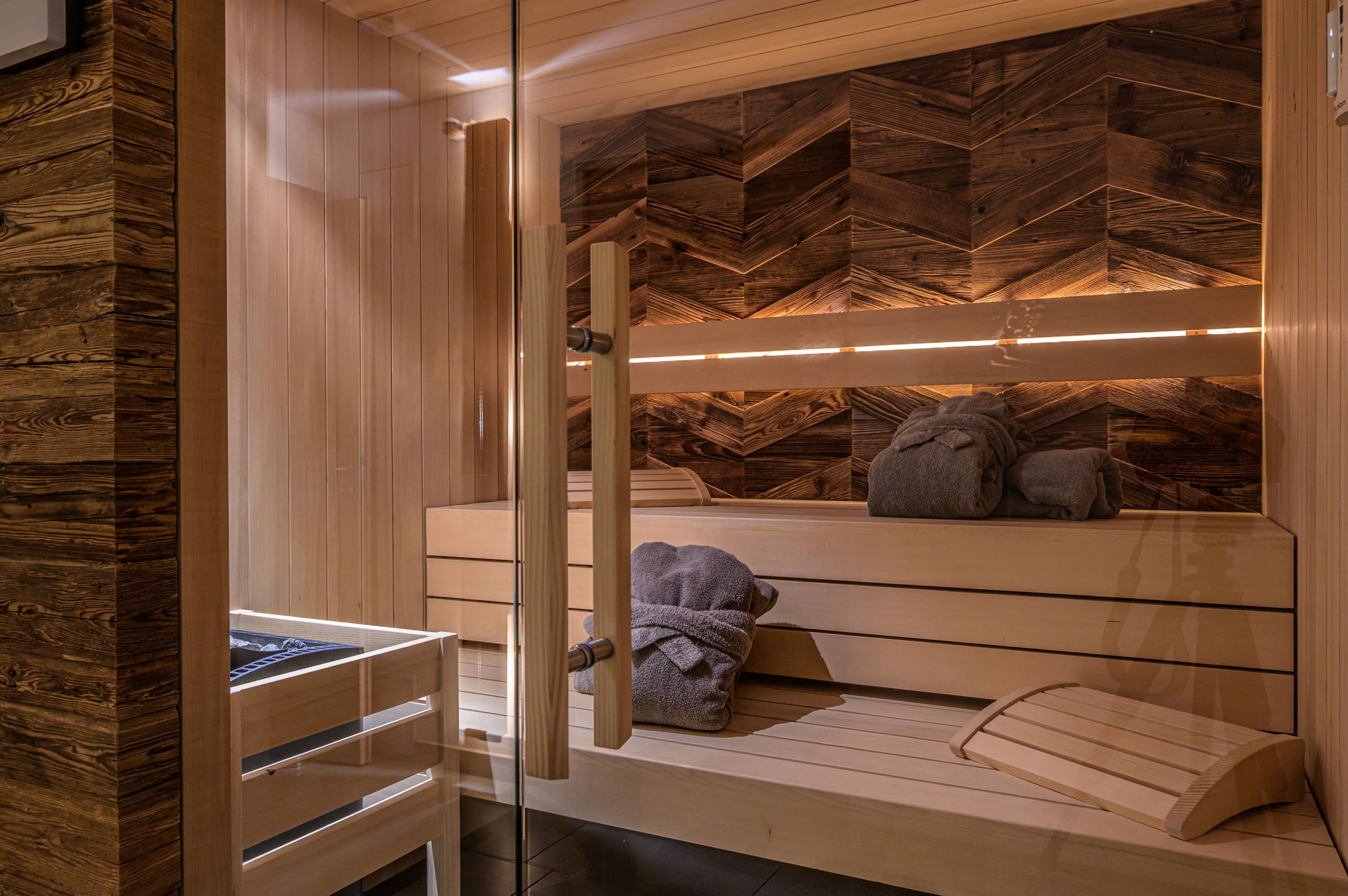 A sauna with wooden benches, a glass door, and a herringbone-patterned wall.