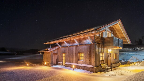 A wooden cabin with a sloped roof, multiple windows, and a bench outside.