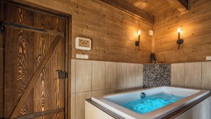 A wooden cabin interior with a hot tub, wooden walls, and a stone mosaic backsplash.