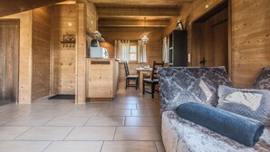 A wooden cabin interior with a dining area, a sofa, and a kitchenette.