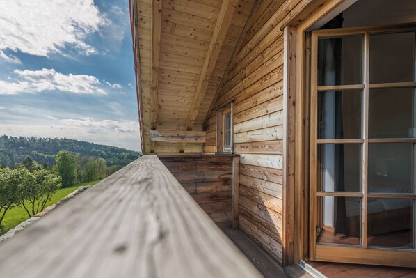 A wooden cabin with a balcony overlooking a forested landscape.
