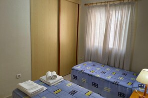 Une petite pièce comprenant un lit, une table de chevet avec une lampe et une fenêtre avec des rideaux.
