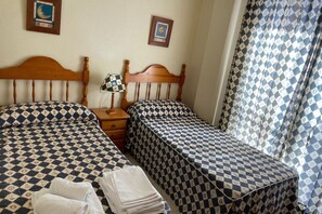 Une chambre d’hôtel avec deux lits, une table de chevet, une lampe et une fenêtre avec des rideaux à motifs.