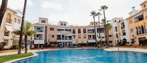 Una piscina rodeada de edificios altos con balcones y palmeras.