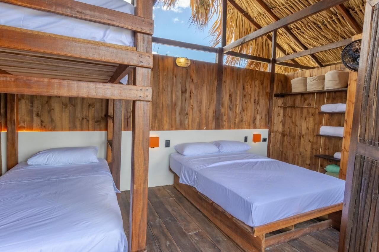 Una habitación rústica de madera con dos literas, techo de paja y un estante con toallas.
