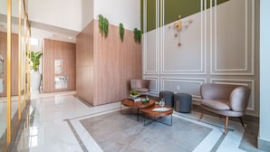 Um lobby moderno com piso de mármore, painéis de madeira e uma área de estar com sofá e poltronas.
