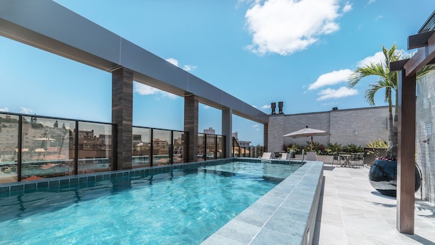 Piscina no terraço com água azul translúcida, cercada por uma barreira de vidro e um deck revestido com azulejos.