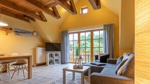 A cozy living room with a sofa, a coffee table, and a dining area with chairs and a table. There is a large window with curtains, a clock on the wall, and a TV in the corner. - Landhaus in Vollerwiek (Vollerwiek)