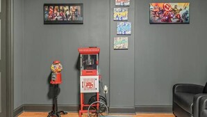 Een kamer met een grijze muur, een knikkerautomaat, een rode en witte popcornkar en stripboekposters.